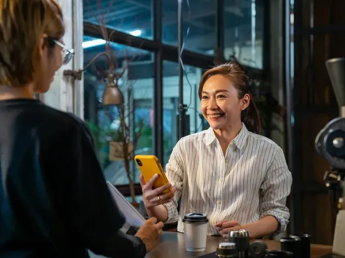 Smiling small business owner with phone talking to customer over coffee inside modern local shop featured on Urban Biz Directory